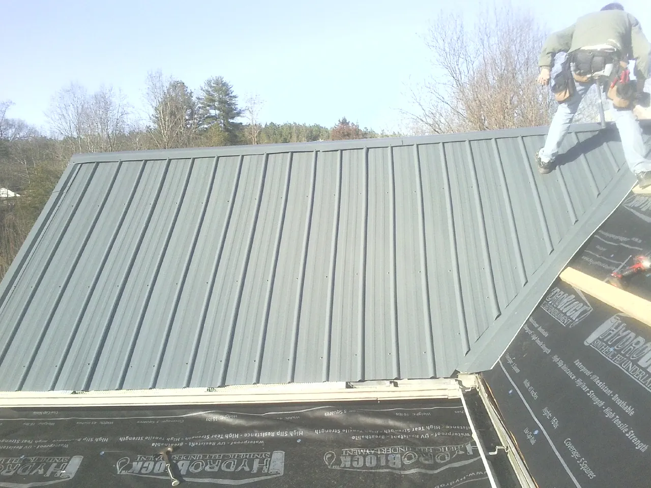 Crew installing dark green standing seam panels over synthetic underlayment in Chanhassen