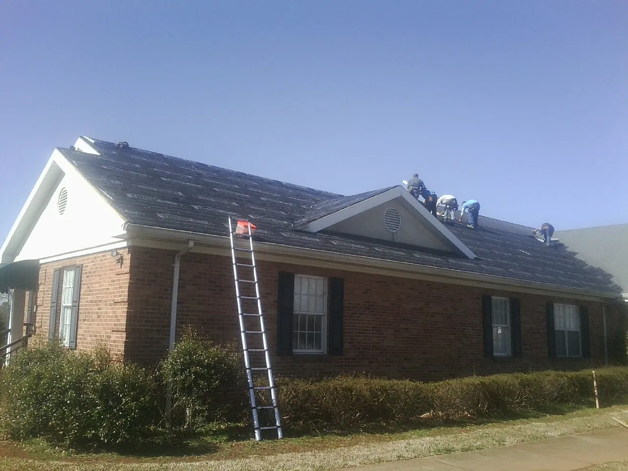 Crew tearing shingles off a brick ranch roof with a ladder set — Emergency Roof Repair work by our crew in Chanhassen