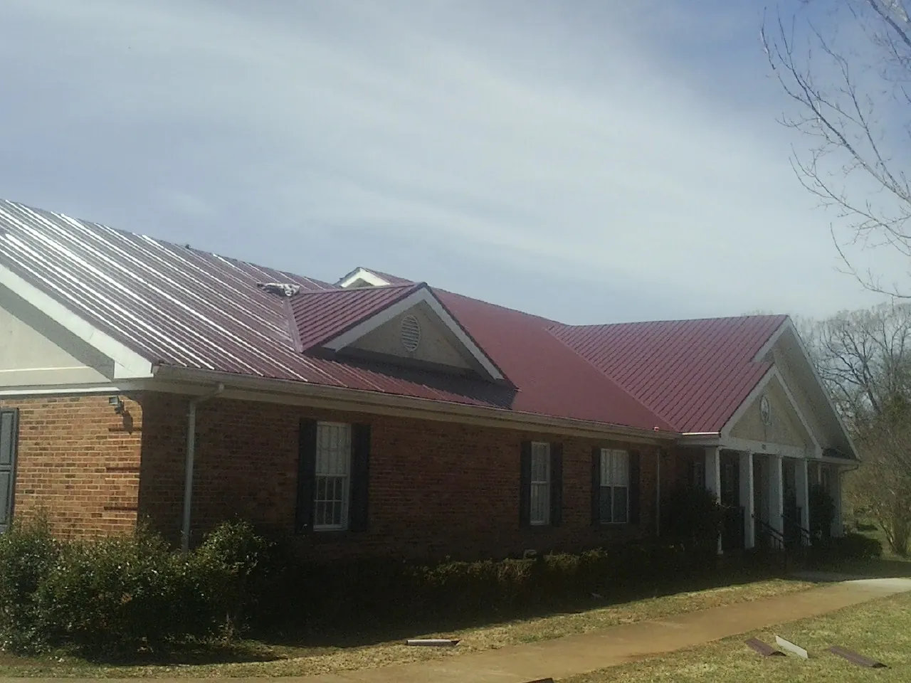 Red metal roof with gabled entries on a long brick building, from a Hail Damage Roof Repair job in Chanhassen