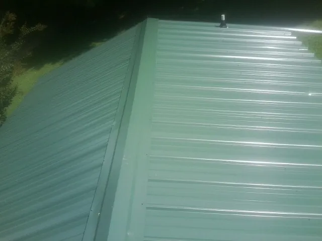 New green metal panels meeting at the ridge of a roof — Flat Roof Repair work by our crew in Chanhassen