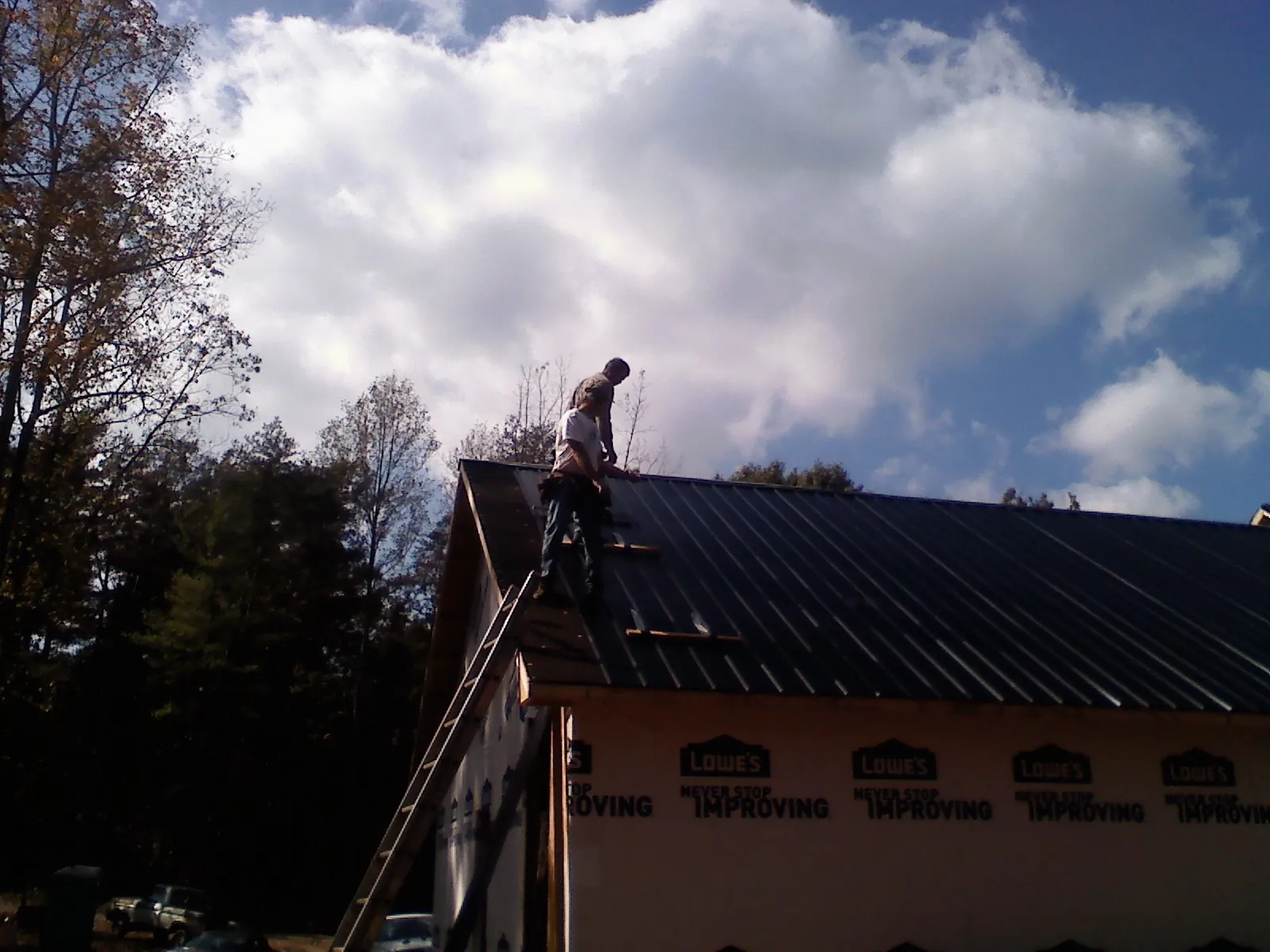 Roofer fastening dark metal panels high against a cloudy sky, from a Roof Inspection job in Chanhassen