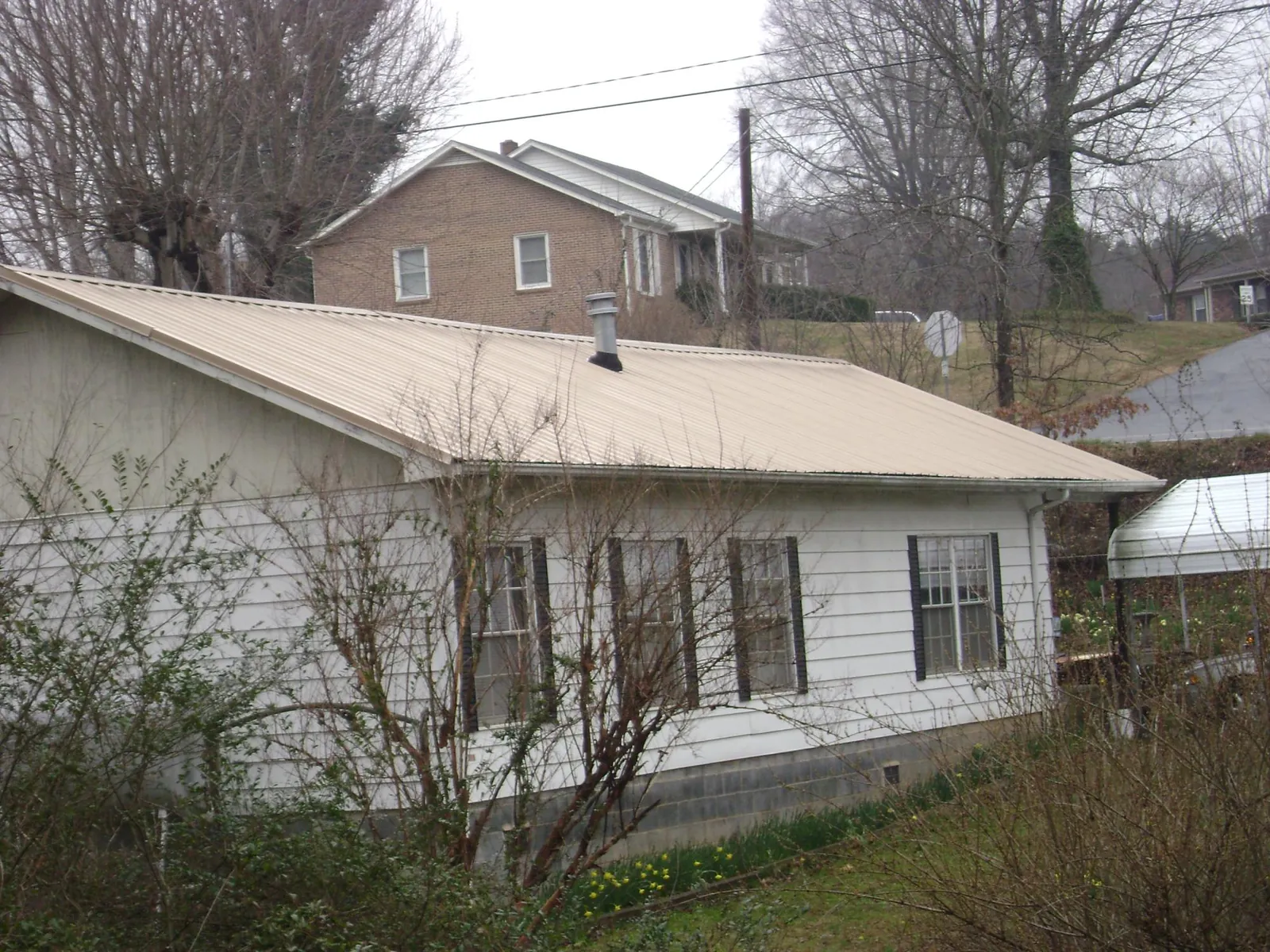 Tan metal roof on a white sided house set into a hillside — Commercial Roofing by Roofing Brothers in Chanhassen